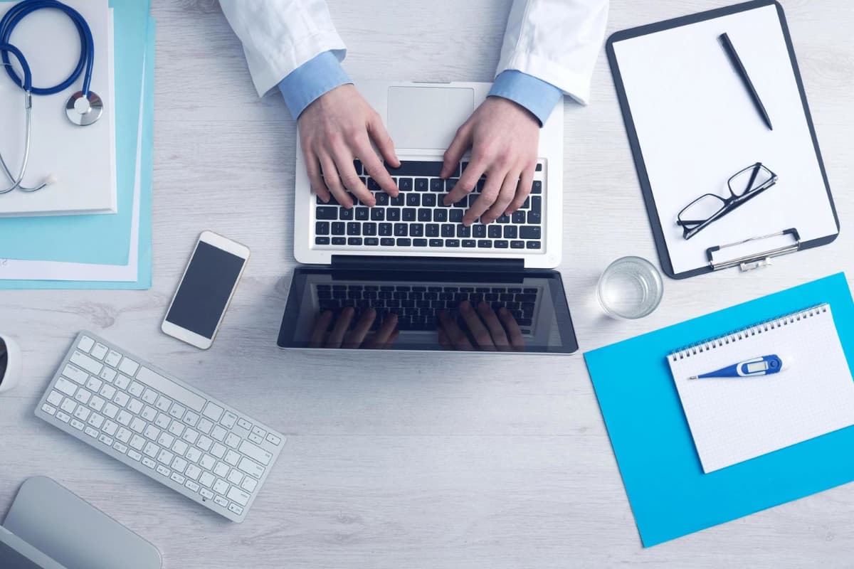 Itens tecnológicos como laptop, celular e teclado, simbolizando a transformação digital na clínica ou consultório médico.