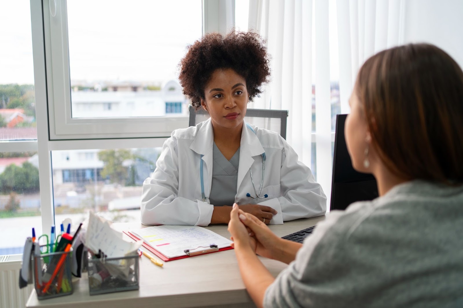 A imagem apresenta um momento de consulta médica, com uma médica e uma paciente em uma conversa.