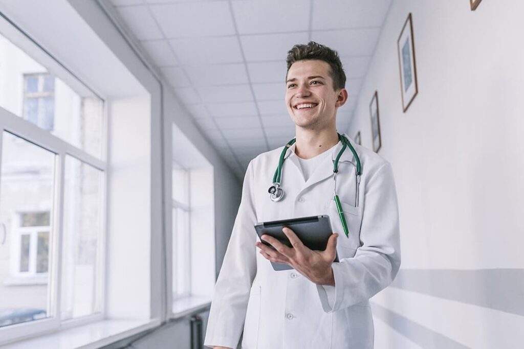 Médico sorridente com tablet na mão, fazendo uma pesquisa de como transformar o consultório em uma clínica médica.