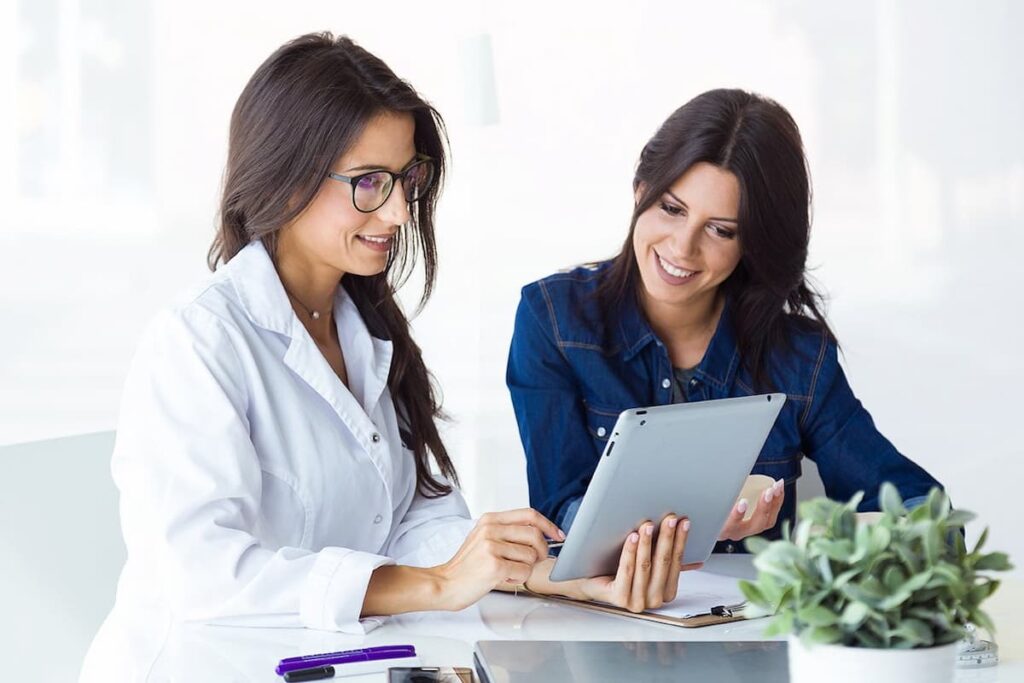 Médica segurando um tablet enquanto faz um atendimento clínico com paciente,