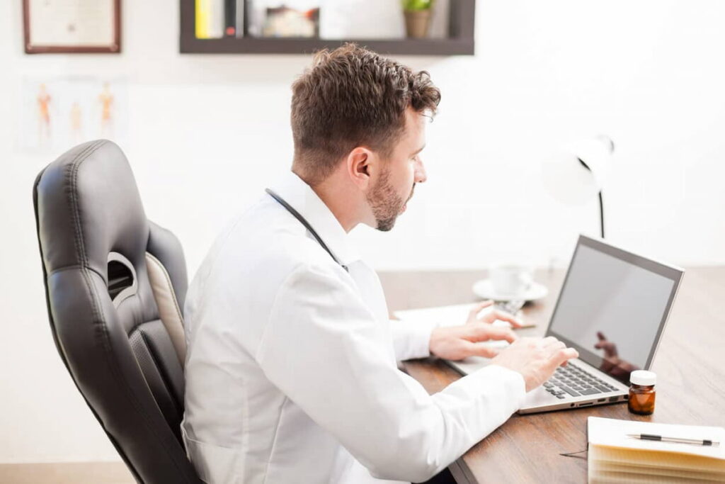 Médico trabalhando em home office com o notebook na mesa.