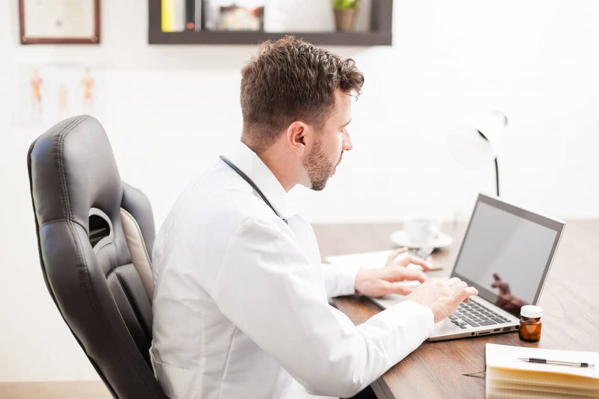 Médico trabalhando em home office com o notebook na mesa.