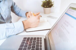 Pessoa trabalhando com laptop e guia TISS ao lado, em um ambiente de escritório claro.