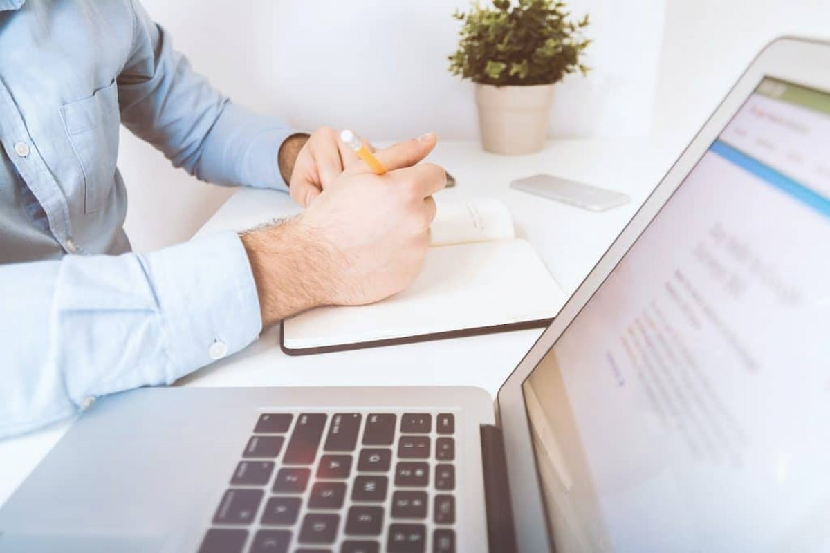 Pessoa trabalhando com laptop e guia TISS ao lado, em um ambiente de escritório claro.