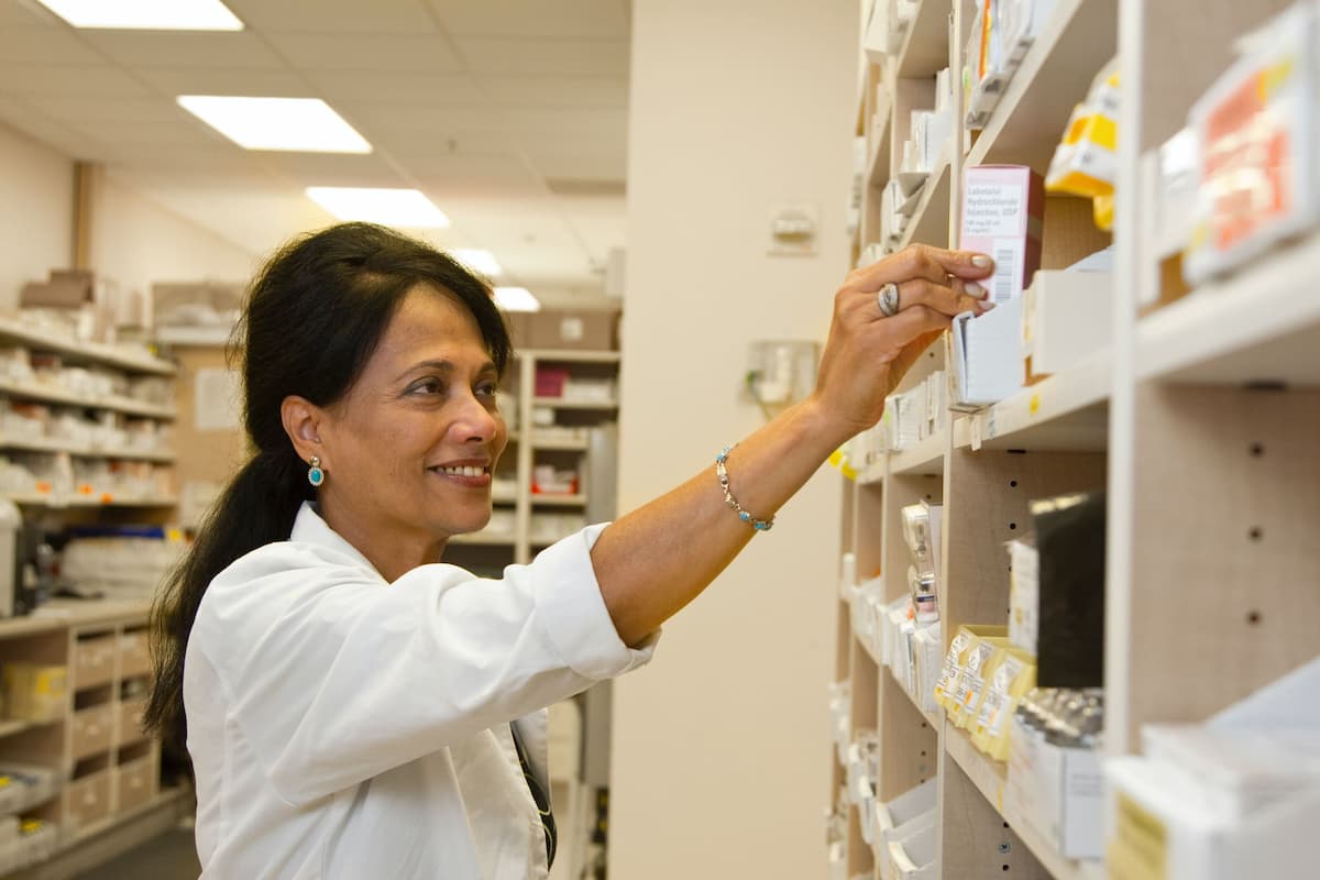 Funcionária de clínica médica organizando medicamentos nas prateleiras, representando gestão de estoque.
