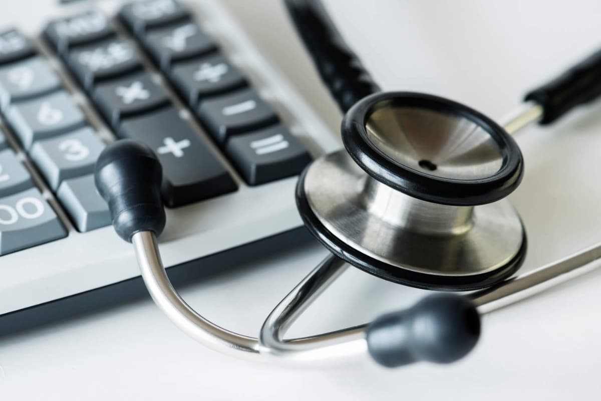 Stetoscópio, calculadora e caneta sobre uma superfície branca, simbolizando faturamento médico.