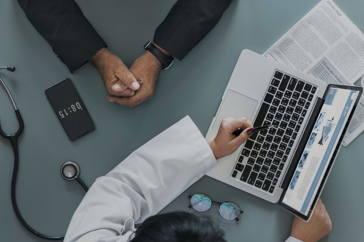 Pessoa utilizando um laptop para cadastro de pré-consulta em um ambiente com equipamentos médicos.