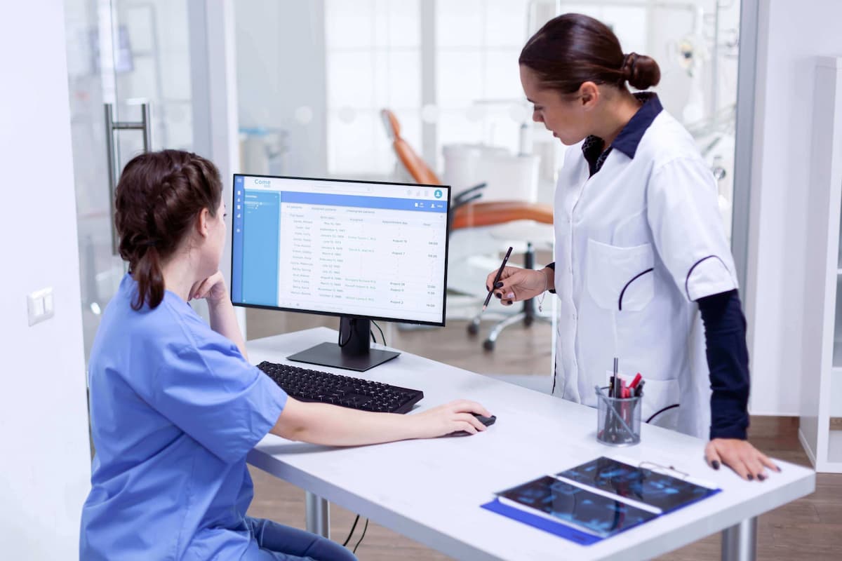 Duas profissionais de saúde fazendo confirmação de consulta médica no computador.