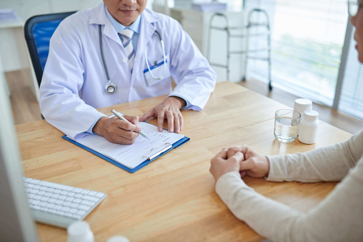 Médico discutindo inovações em saúde com paciente em clínica, com equipamentos médicos e documentos na mesa.