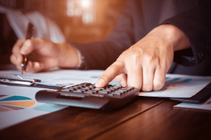Pessoa fazendo cálculos com calculadora e papéis. Imagem ilustrativa para texto ebitda o que é.