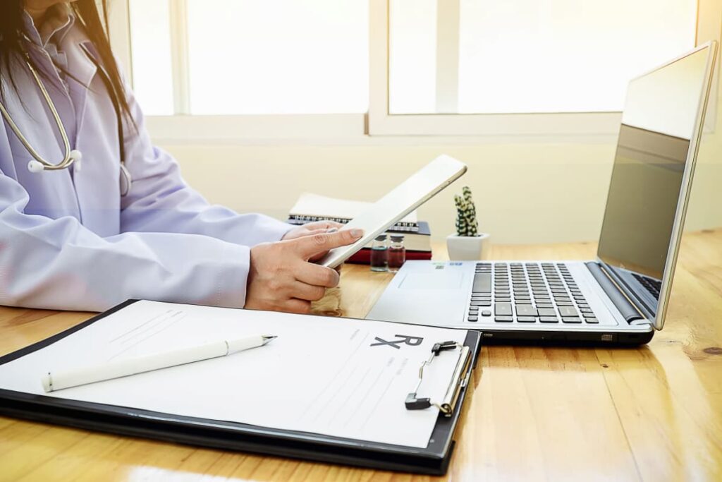 Médica com tablet e notebook, criando um lembrete de consulta médica para pacientes.