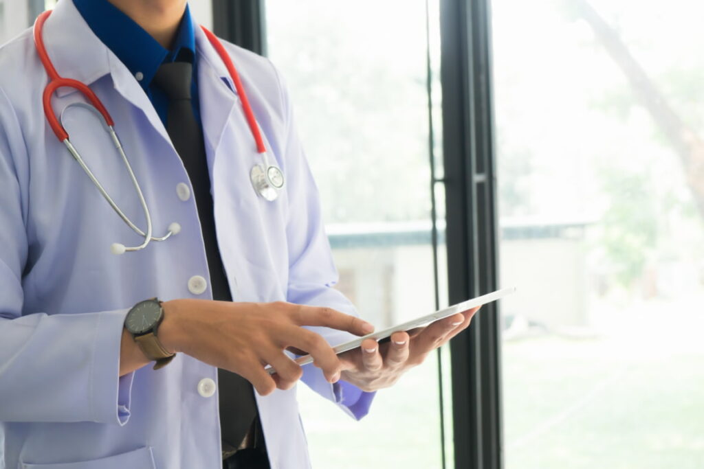 Médico com estetoscópio usando tablet, representando um sistema de saúde digital.