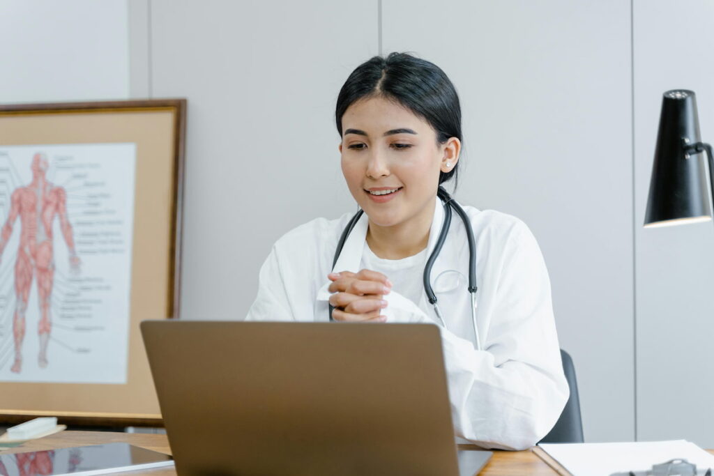Médico em um consultório com um laptop, sugerindo o uso de uma agenda médica.