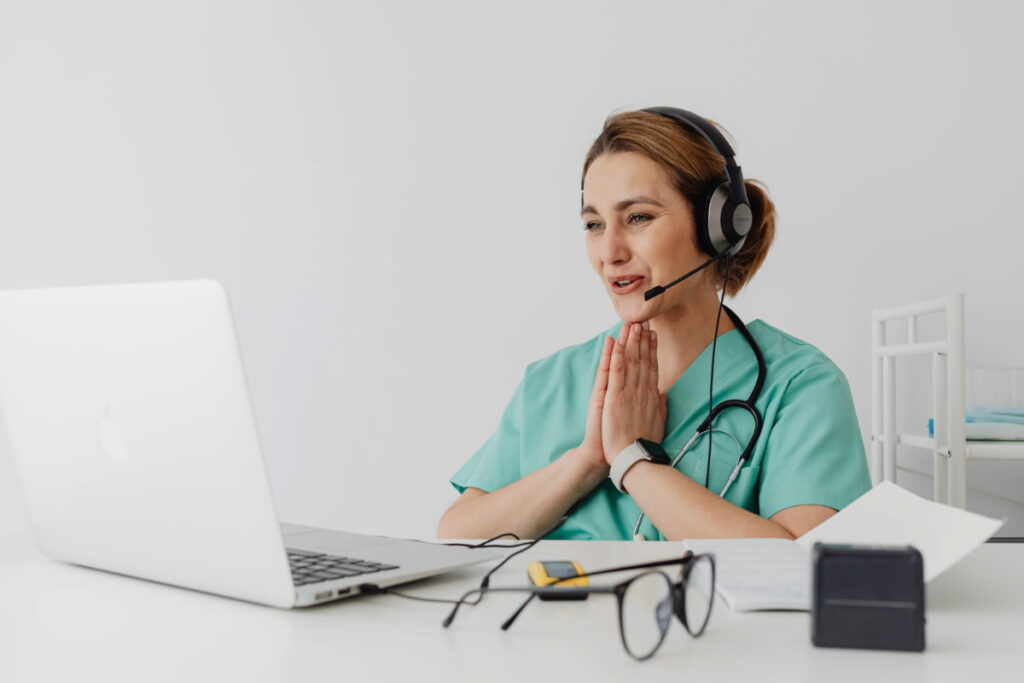Profissional de saúde usando laptop, fone e estetoscópio, exemplificando como trabalhar com telemedicina.