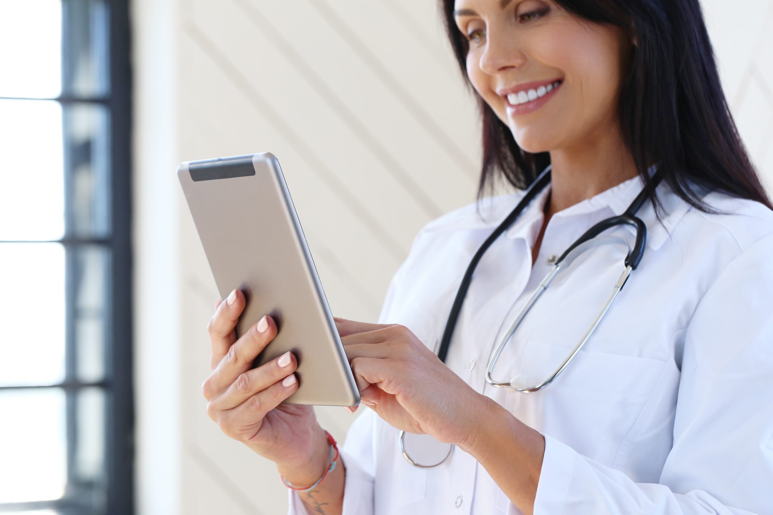 Tecnologia na medicina: médica com estetoscópio no pescoço jacelo branco, com sorriso no rosto ela possui um tablet em suas mãos