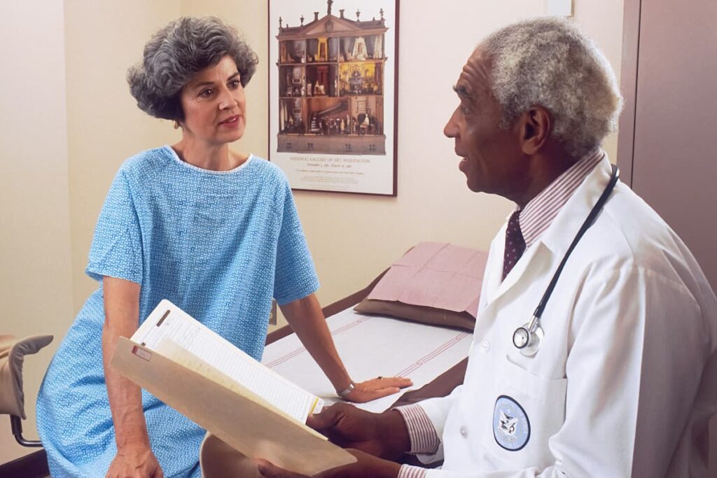 Fotografia de um médico que conversa com uma paciente no consultório médico.
