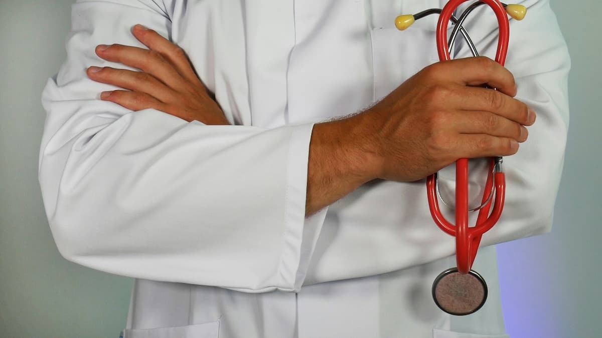 Fotografia de um homem, vestindo uma bata de médico, de braços cruzados.