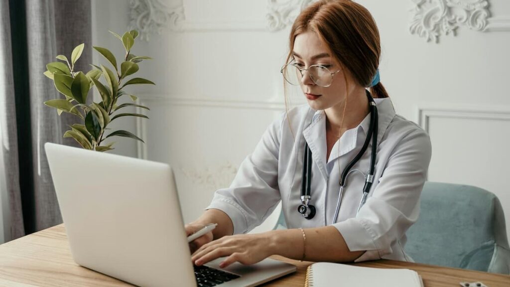 Fotografia de uma médica analisando o prontuário eletrônico de um paciente em seu notebook.