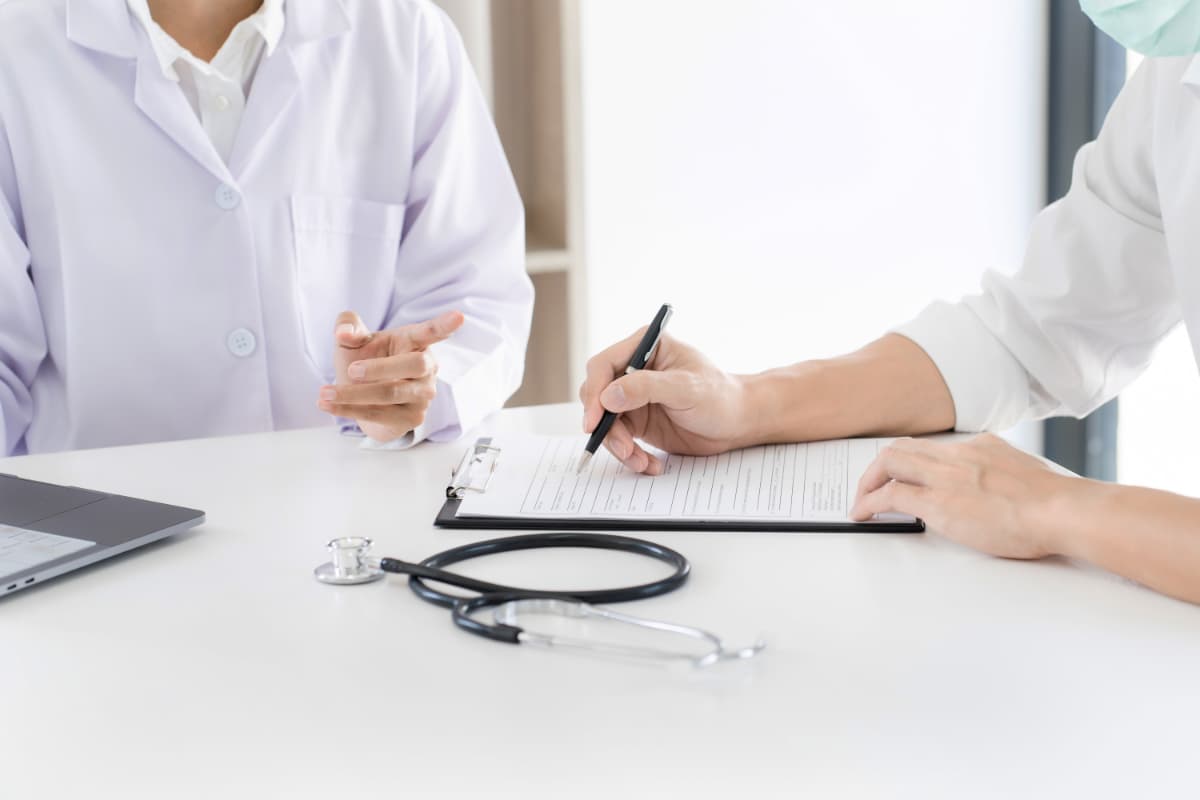 Um profissional de saúde com jaleco branco está preenchendo um documento de encaminhamento médico ao lado de um paciente.