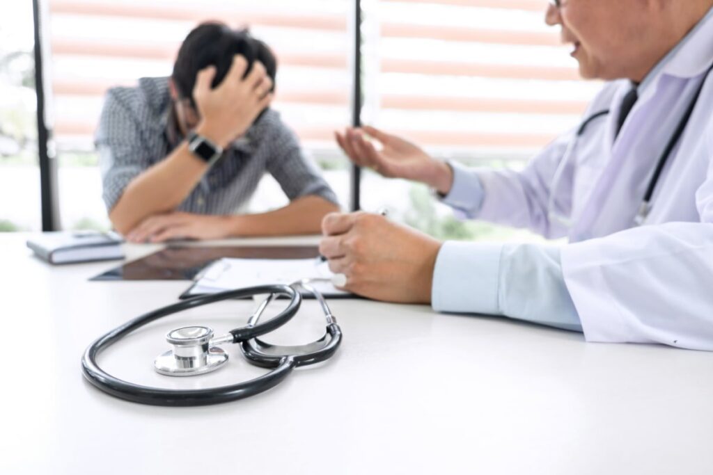 Paciente angustiado com médico, estetoscópio na mesa, sugere erro médico.