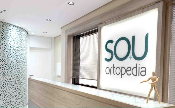 Sala de escritório médico da SOU Ortopedia, com um telão branco com o nome da empresa escrito em verde.