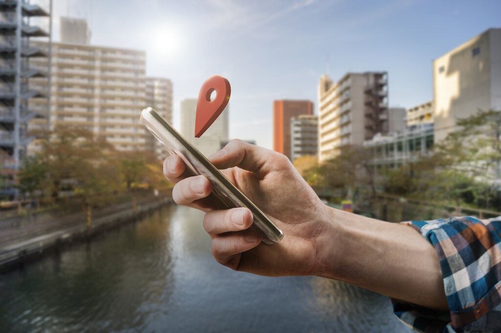 Pessoa segurando um celular com a mão direita, onde tem um marcador vermelho de localização.
