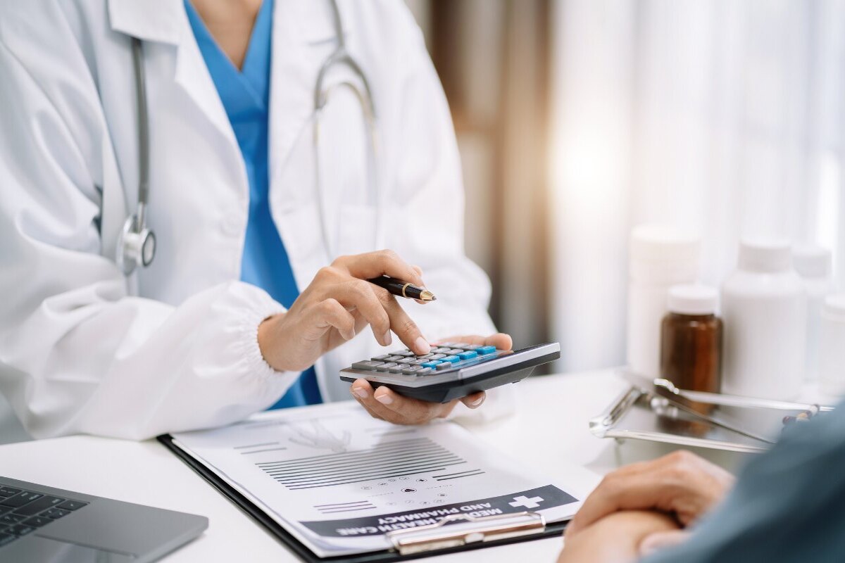 uma médica de jaleco branco faz as contas das despesas médicas para um paciente com uma calculadora