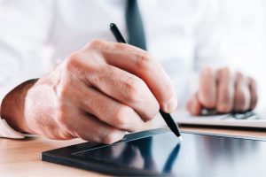 Mão assinando digitalmente em tablet, representando a assinatura digital nos prontuários médicos com tecnologia moderna.
