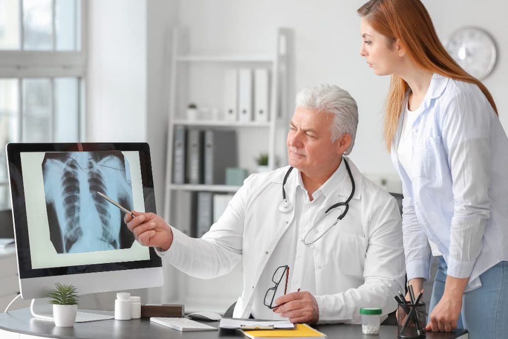 Médico explicando radiografia a paciente em consulta, ilustrando a jornada do paciente no diagnóstico e acompanhamento médico.