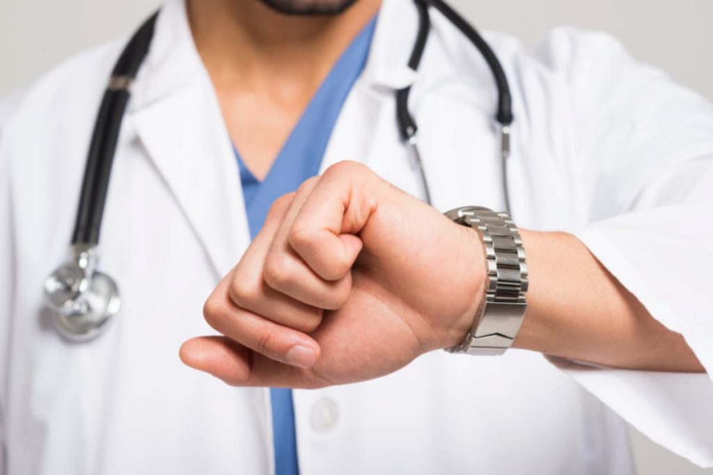 Médico verificando o relógio, representando o impacto do no-show em clínica médica devido à ausência de pacientes agendados.