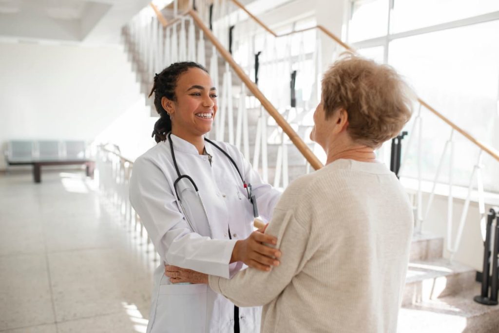 Médica sorridente acolhendo paciente idosa no hospital, representando um retorno de consulta com cuidado e empatia.