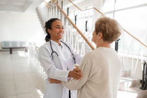 Médica sorridente acolhendo paciente idosa no hospital, representando um retorno de consulta com cuidado e empatia.