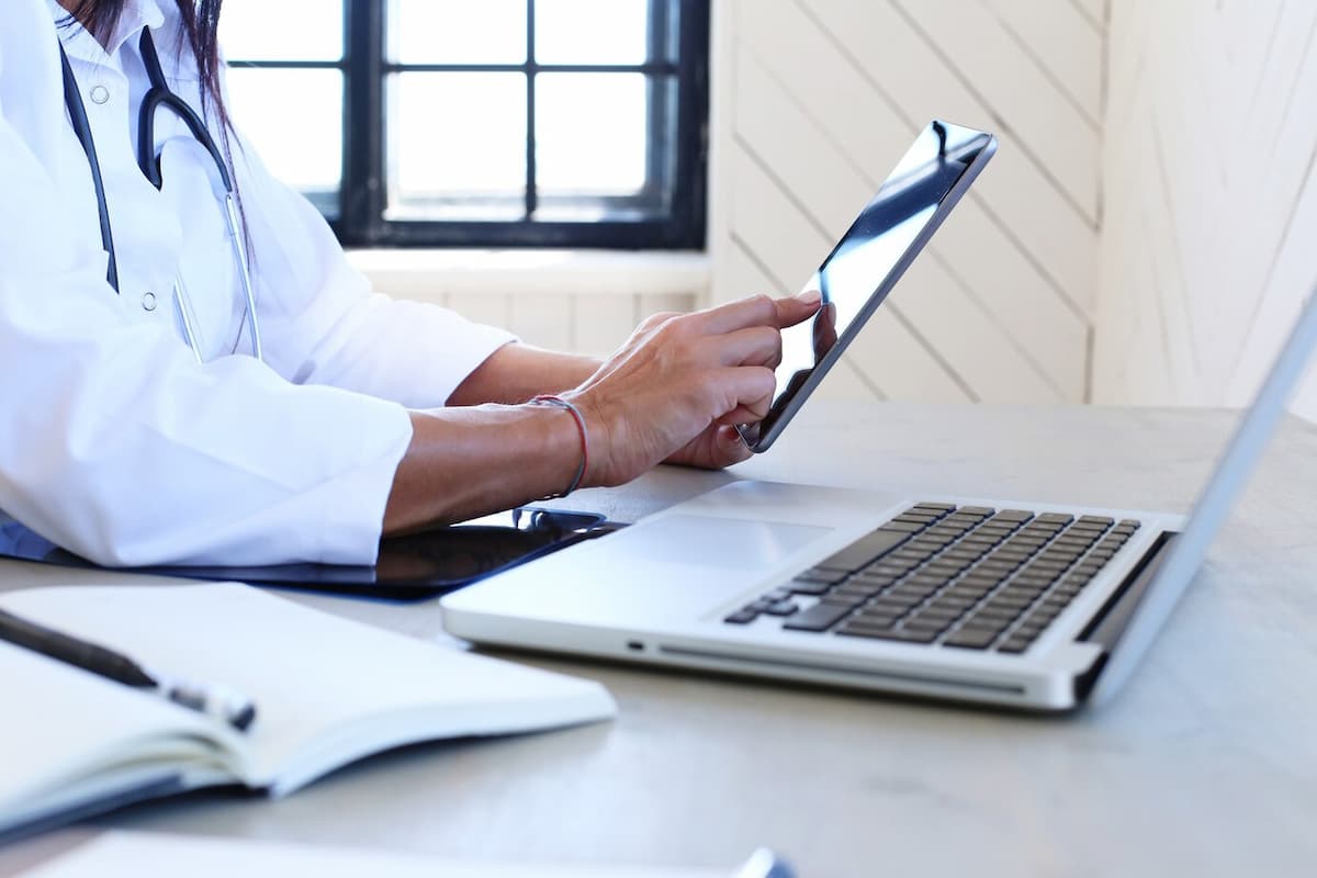 Médico analisando informações em tablet e laptop, representando a eficiência da Cobrança Inteligente do Conclínica.