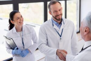 Médico cumprimentando duas pessoas, simbolizando uma negociação em saúde e colaboração profissional.