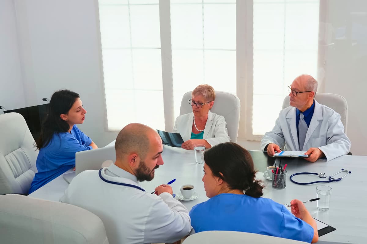 Reunião de junta médica com profissionais analisando exames e discutindo casos clínicos em uma sala de conferência.