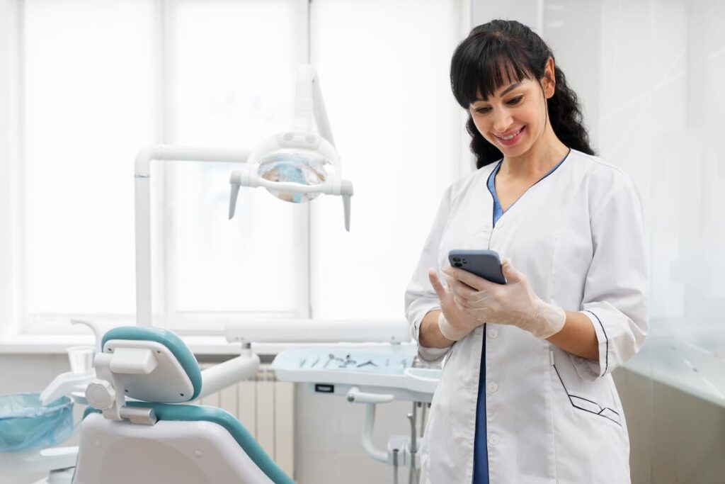 Dentista usando o melhor software para clínicas odontológicas no celular, em um consultório moderno e bem equipado.