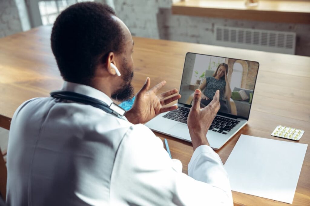 Médico realiza telediagnóstico em consulta online, conversando com paciente por videochamada em um ambiente iluminado.
