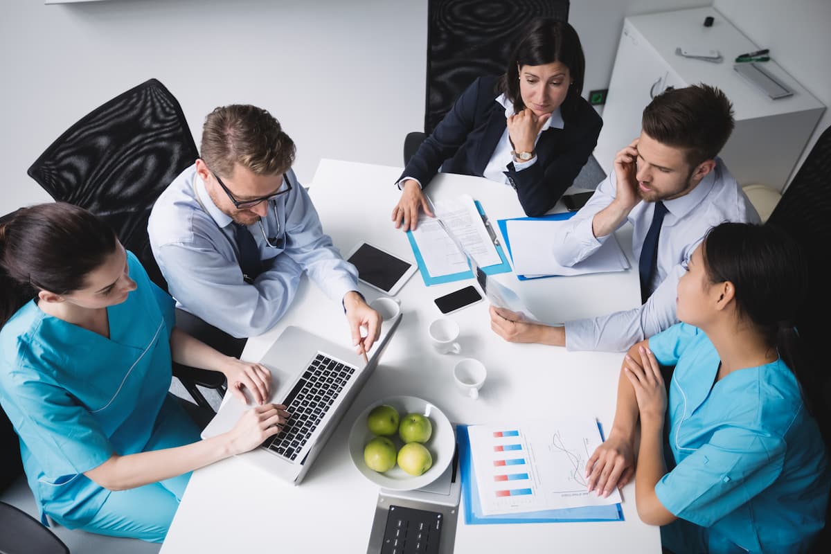 Várias pessoas ao redor de uma mesa com um laptop, conversando sobre como funciona um coworking médico.