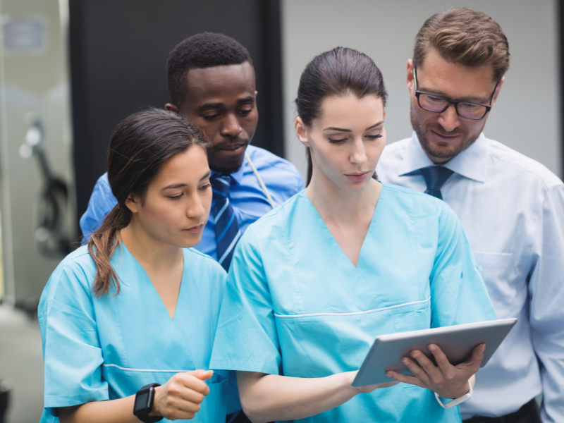 O arquivo de imagem enviado mostra um grupo de quatro profissionais, provavelmente da área da saúde ou executiva, olhando para uma tablet digital.