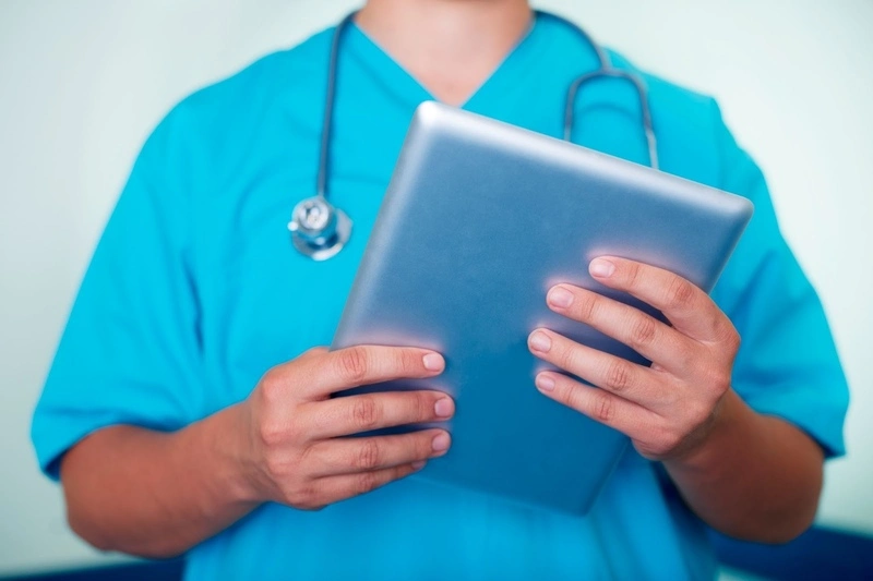 enfermeiro de uniforme azul segurando um tablet para visualizar um prontu&aacute;rio eletr&ocirc;nico interoper&aacute;vel