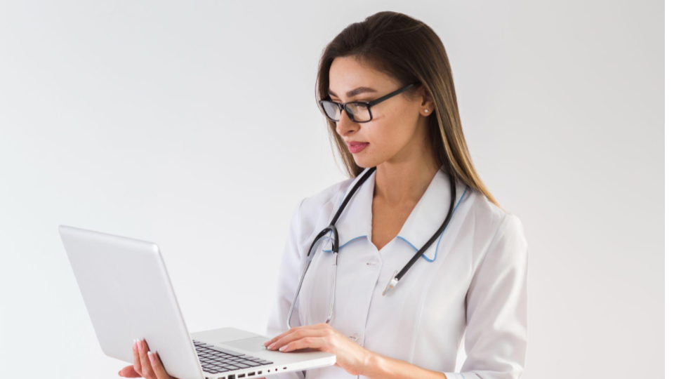 A imagem mostra uma profissional da área da saúde, vestida com jaleco branco e estetoscópio no pescoço, utilizando um notebook.