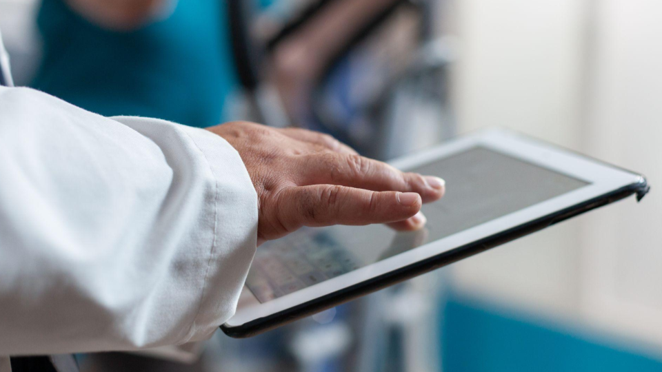A imagem mostra um close-up de uma mão tocando a tela de um tablet, sugerindo o uso de tecnologia em um contexto profissional de software médico.