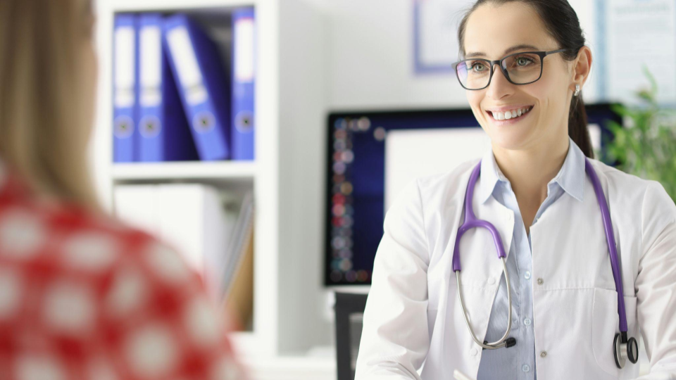 A imagem mostra uma profissional da área da saúde, provavelmente uma médica, em um consultório.