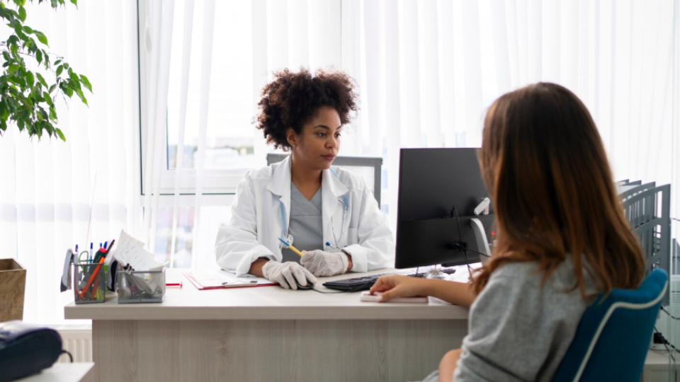 A imagem retrata um cenário de atendimento médico ou consulta clínica, destacando a interação profissional e humanizada entre uma médica e sua paciente.