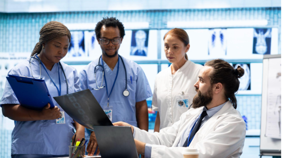 Esta imagem retrata uma equipe médica multidisciplinar reunida em um ambiente hospitalar tecnológico para analisar exames e discutir um caso clínico.