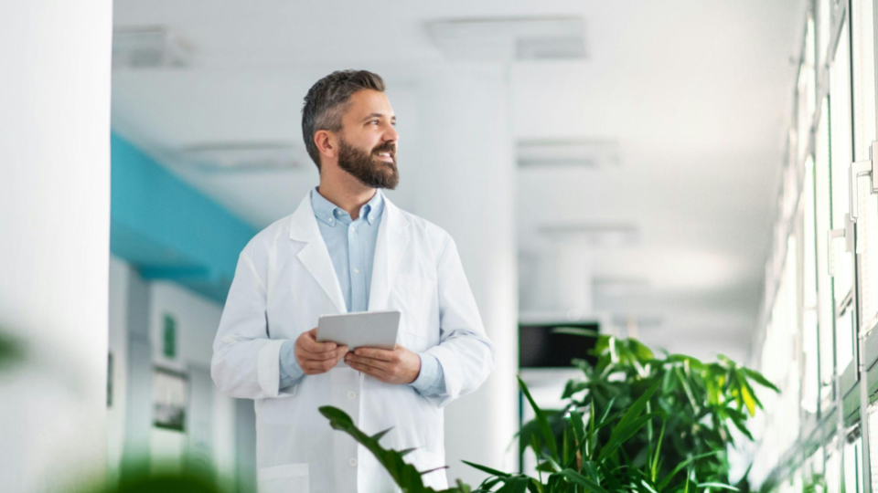 Médico em ambiente hospitalar utilizando um tablet para analisar informações clínicas e dados de pacientes, representando o uso de tecnologia na gestão de sistemas de saúde e na rotina médica sem interrupção da operação.