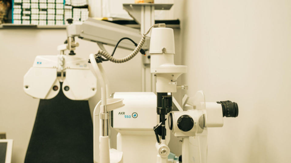 A imagem mostra o interior de um consultório oftalmológico ou optometria, equipado com instrumentos profissionais para exames de vista.