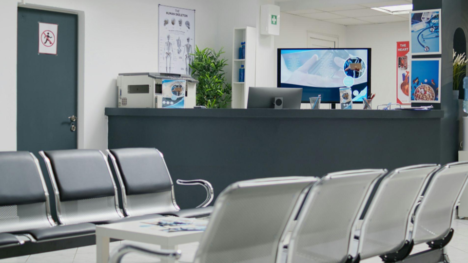 Esta imagem mostra a recepção e sala de espera de um centro médico ou clínica de saúde, moderna e organizada, no momento sem pacientes ou atendentes.