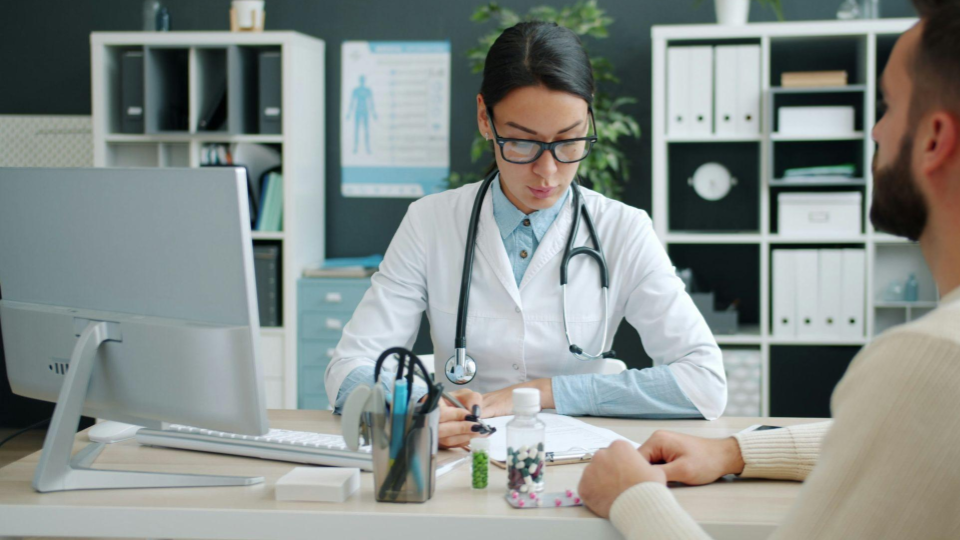 A imagem mostra uma consulta médica em um consultório bem iluminado e organizado.