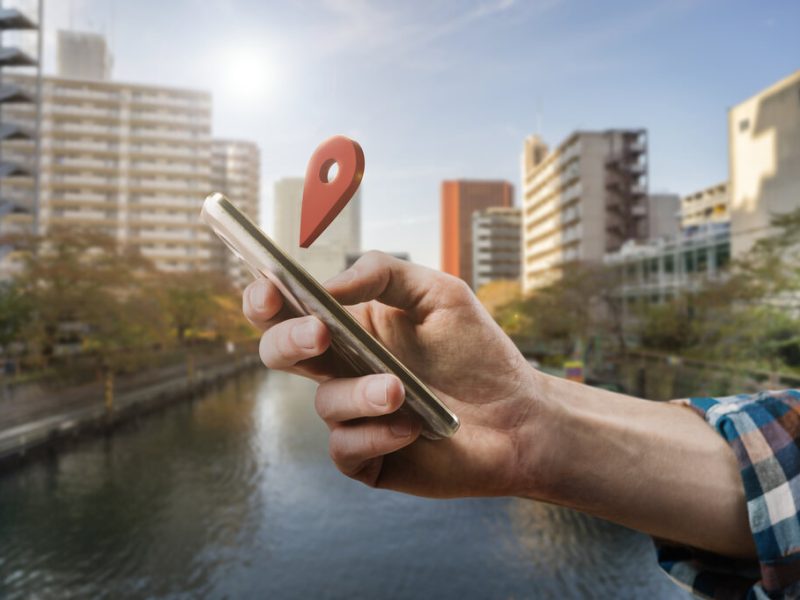 Pessoa segurando um celular com a mão direita, onde tem um marcador vermelho de localização.